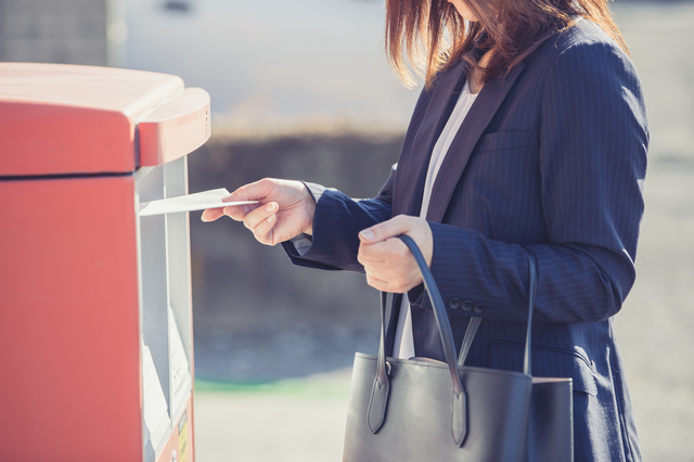 スーツ姿の女性がポストに手紙を投函